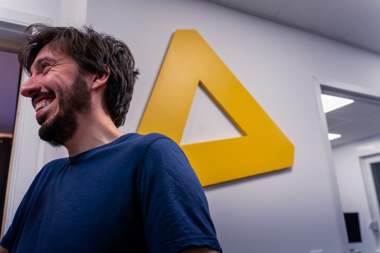 Membre du coworking Neodelta souriant devant le triangle jaune de la marque, dans les locaux de Longeville-lès-Metz